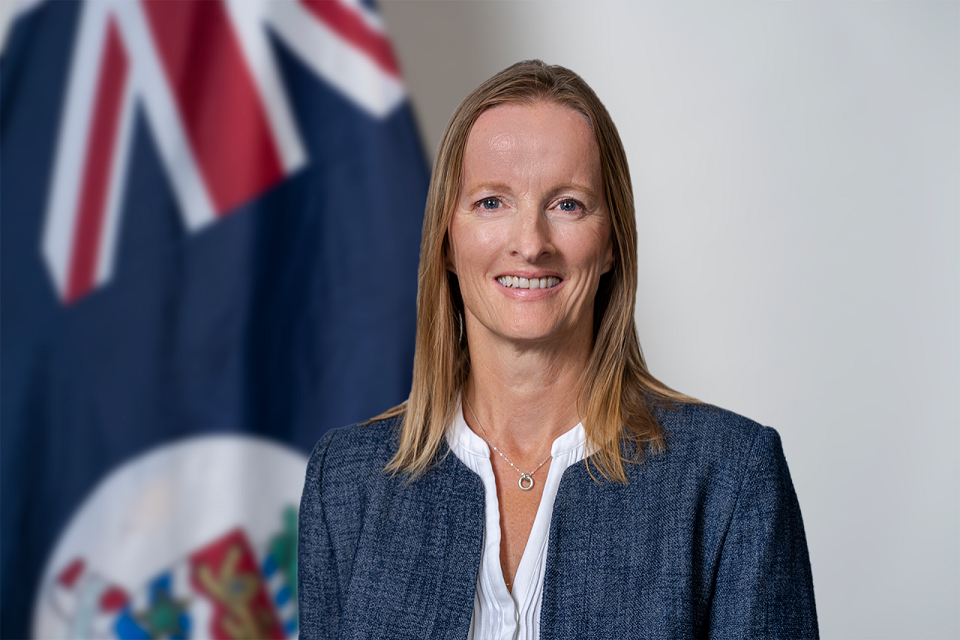 Woman smiling headshot with Cayman Islands flag in background.