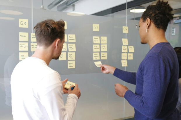 2 people standing in front of a glass wall covered in post-it stickers
