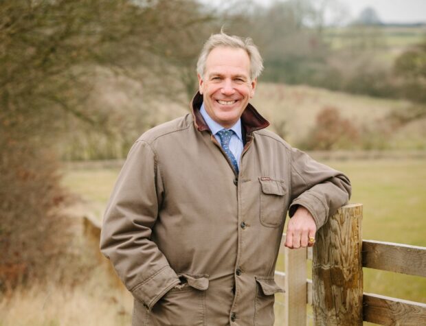 A man stands against a fence smiling into the camara