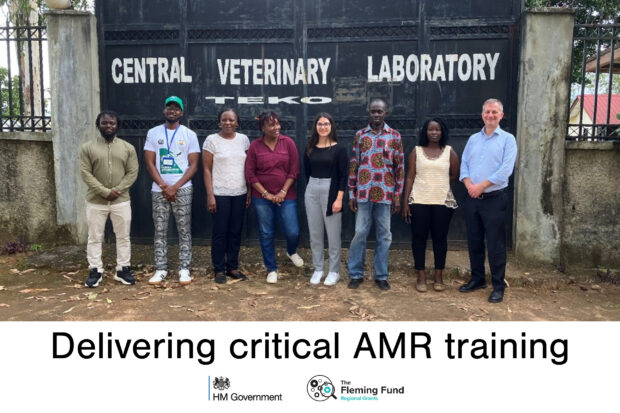Eight individuals standing in front of a large black gate with, "Central Veterinary Laboratory