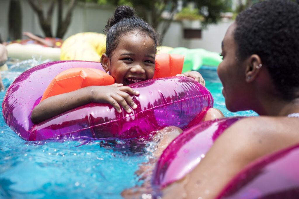 Young girl playing with her mother in a swimming pool, floating in a large, pink inflatable ring