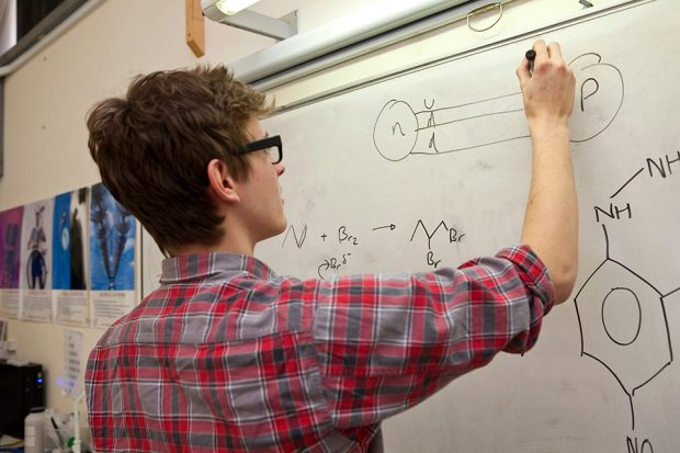 A student drawing chemical notations on a whiteboard