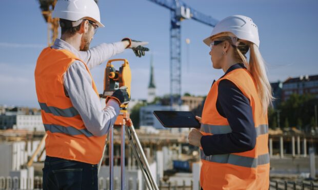 Two surveyors in high visibility jackets, overseeing a housing construction site
