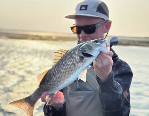 Ben Lovell by the coast in his angling gear holding a fish