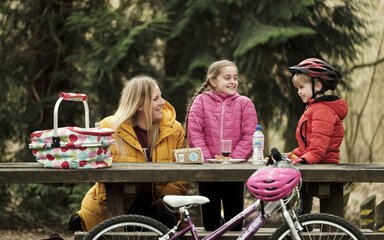 A young family sat on a wooden bench having a picnic in the forest