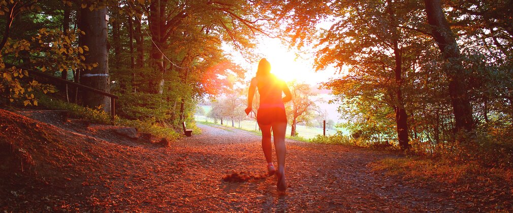 Woman running towards sunset in the forest, autumnal forest