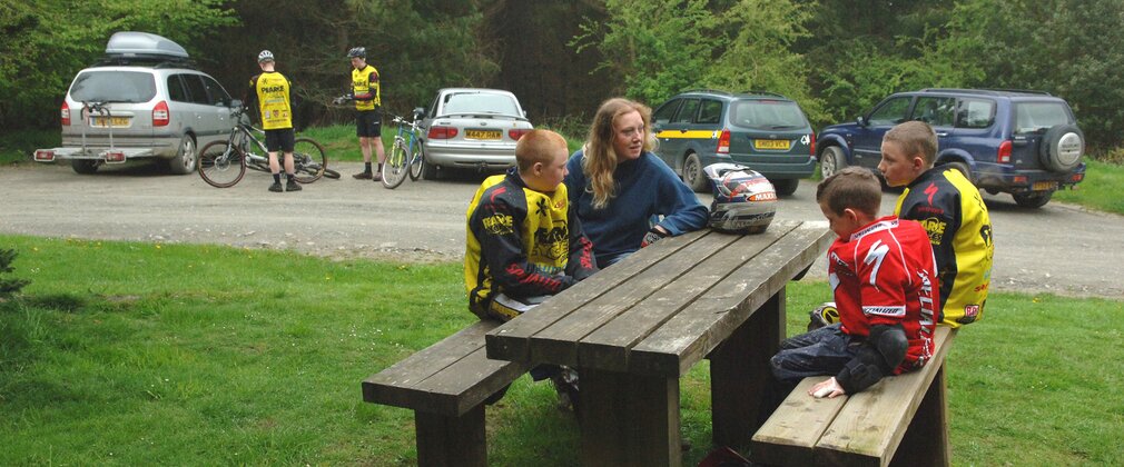People wearing mountain biking gear are sat at a picnic table at Hopton Wood