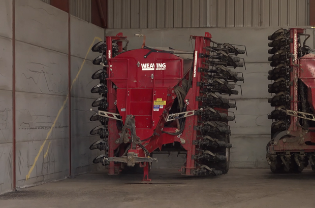 A direct drill, red in colour situated in farm building with grey floors and walls