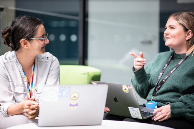 Two people working on laptops having a conversation.