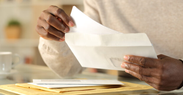 A black person's hands opening a white letter