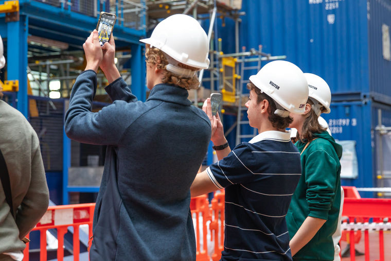 Visitors in white hard hats at UKAEA take photos fusion energy machines.