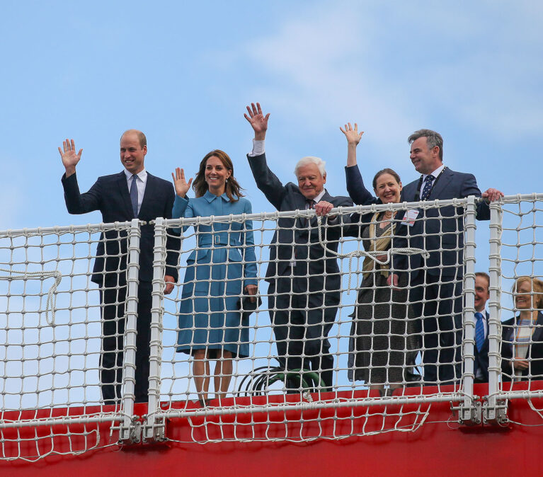Prince William, Duke of Cambridge, David Attenborough et al. waving from bow of the research ship Sir David Attenborough.