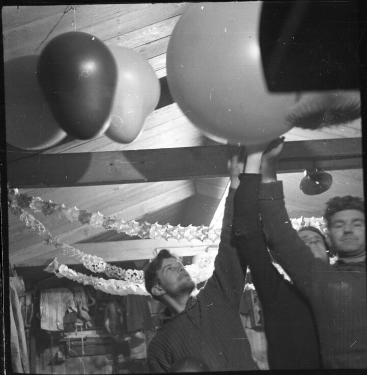A black and white photo of 3 men decorating a room with balloons