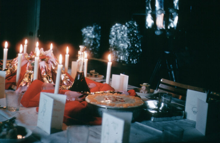 A long dinner table decorated with cards, candles and a cake.