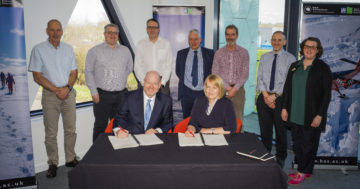 A group of business people signing a business contract with colleagues in the background