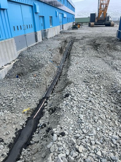 A line of track for a cable along a rubbly ground surface next to a bright blue building with a construction vehicle in the background.