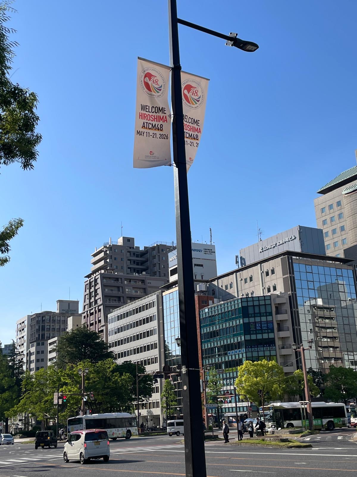 A street view of Hiroshima on a sunny day, with a flyer attached to a lamppost advertising the ATCM.