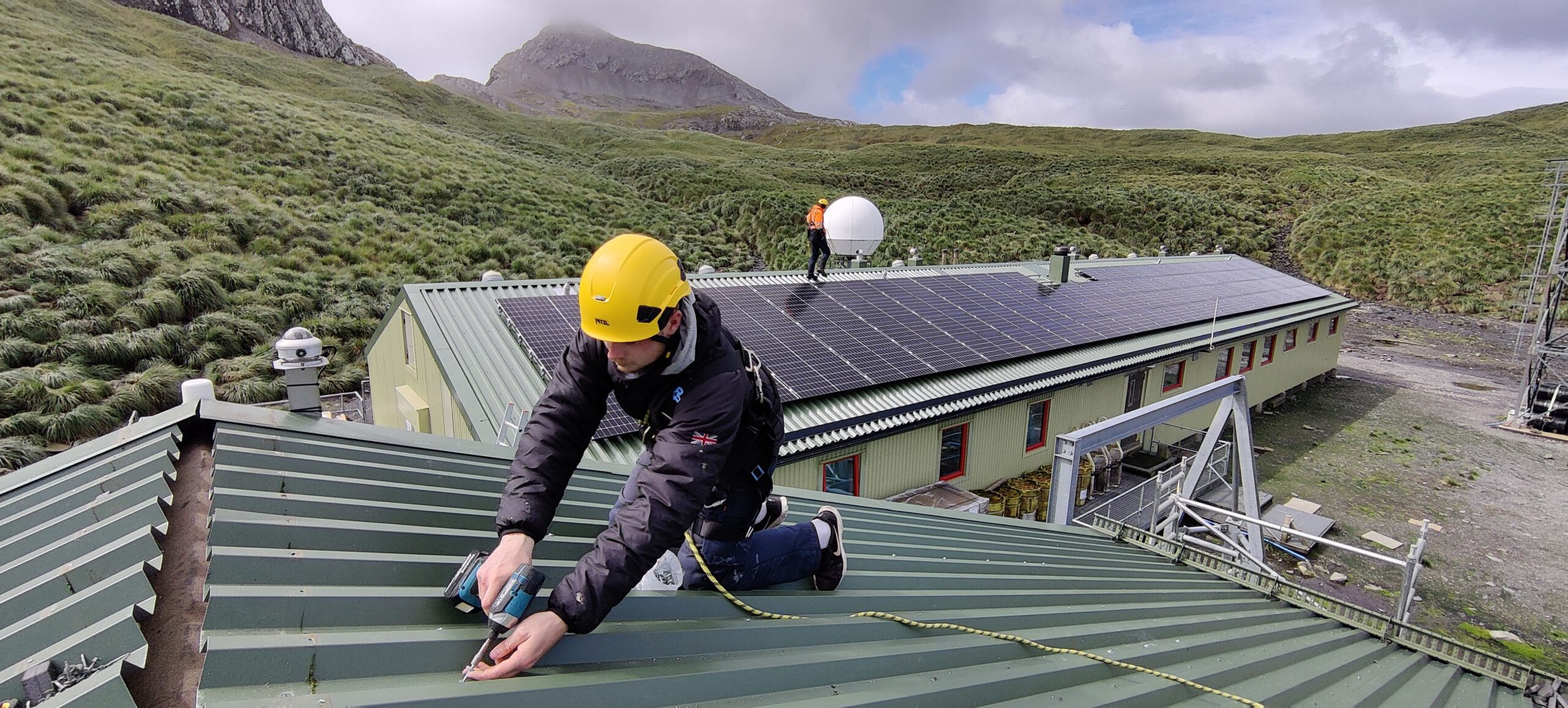 A man on top of a roof covering in solar energy panels with a mountain in the background.