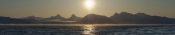 A sunset over a body of water with a mountain in the background.