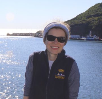 A person wearing sunglasses standing in front of a body of water