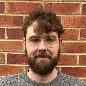 A man wearing glasses and a brick wall