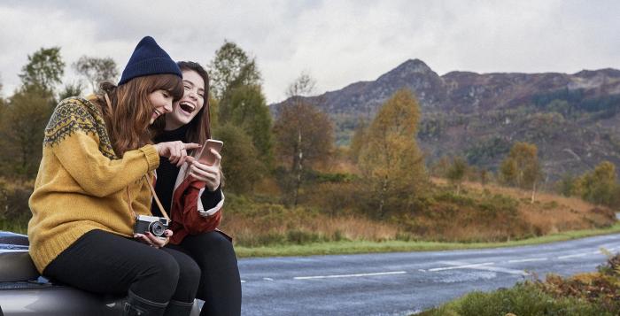 Ladies sat on car bonnet looking and taking photos of the mountains