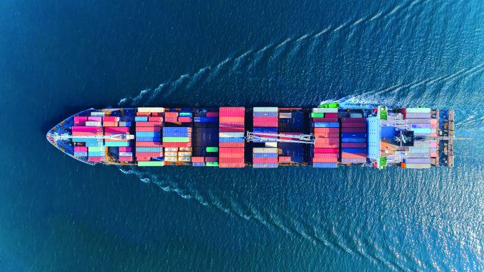 Aerial view of a large cargo ship loaded with colorful shipping containers sailing on the open sea through a clean tyne shipping corridor.