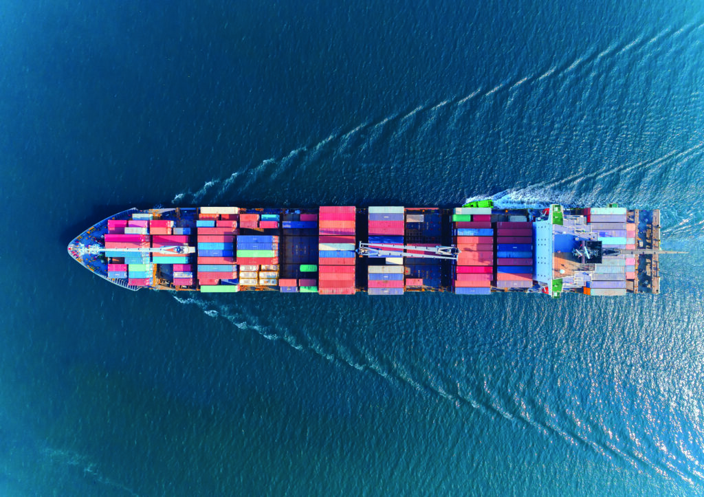 Aerial view of a large cargo ship loaded with colorful shipping containers sailing on the open sea through a clean tyne shipping corridor.