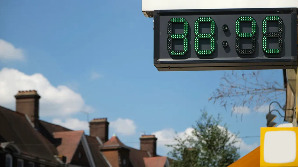 A digital screen shows the temperature reading of 38 degrees celsius. In the background there is a blue sky and rooftops of houses.
