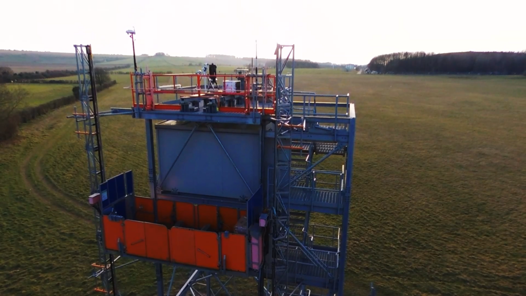 Metal tower structure with platforms and railings in an open field under a clear sky.