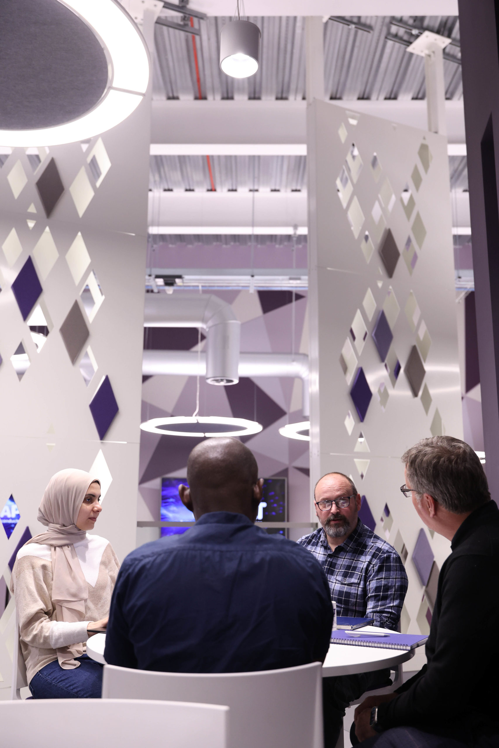 Four people sit around a table having a discussion in a modern, geometric-designed office space. - CSA Catapult