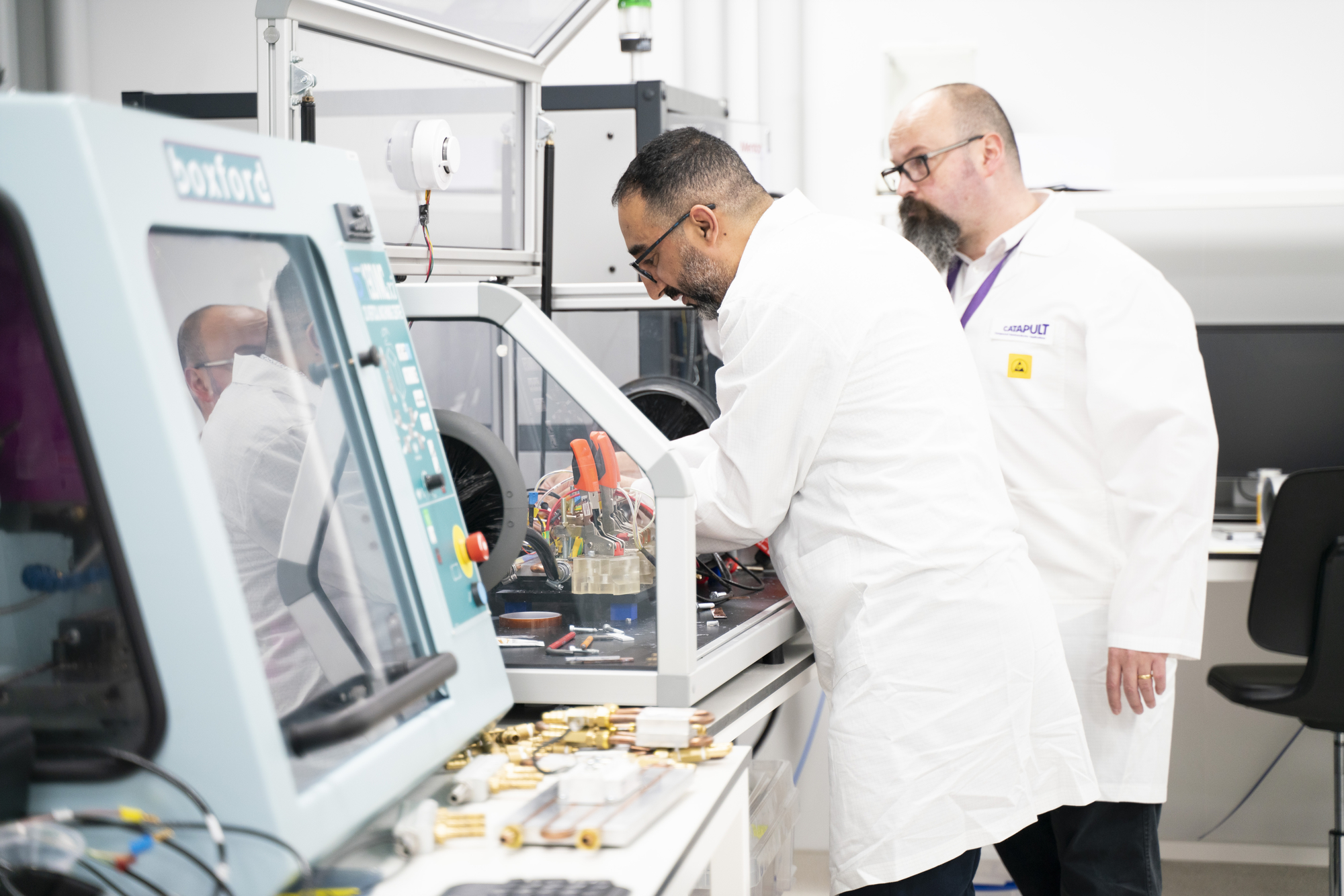 Two scientists in lab coats work with equipment and instruments on a laboratory bench. - CSA Catapult