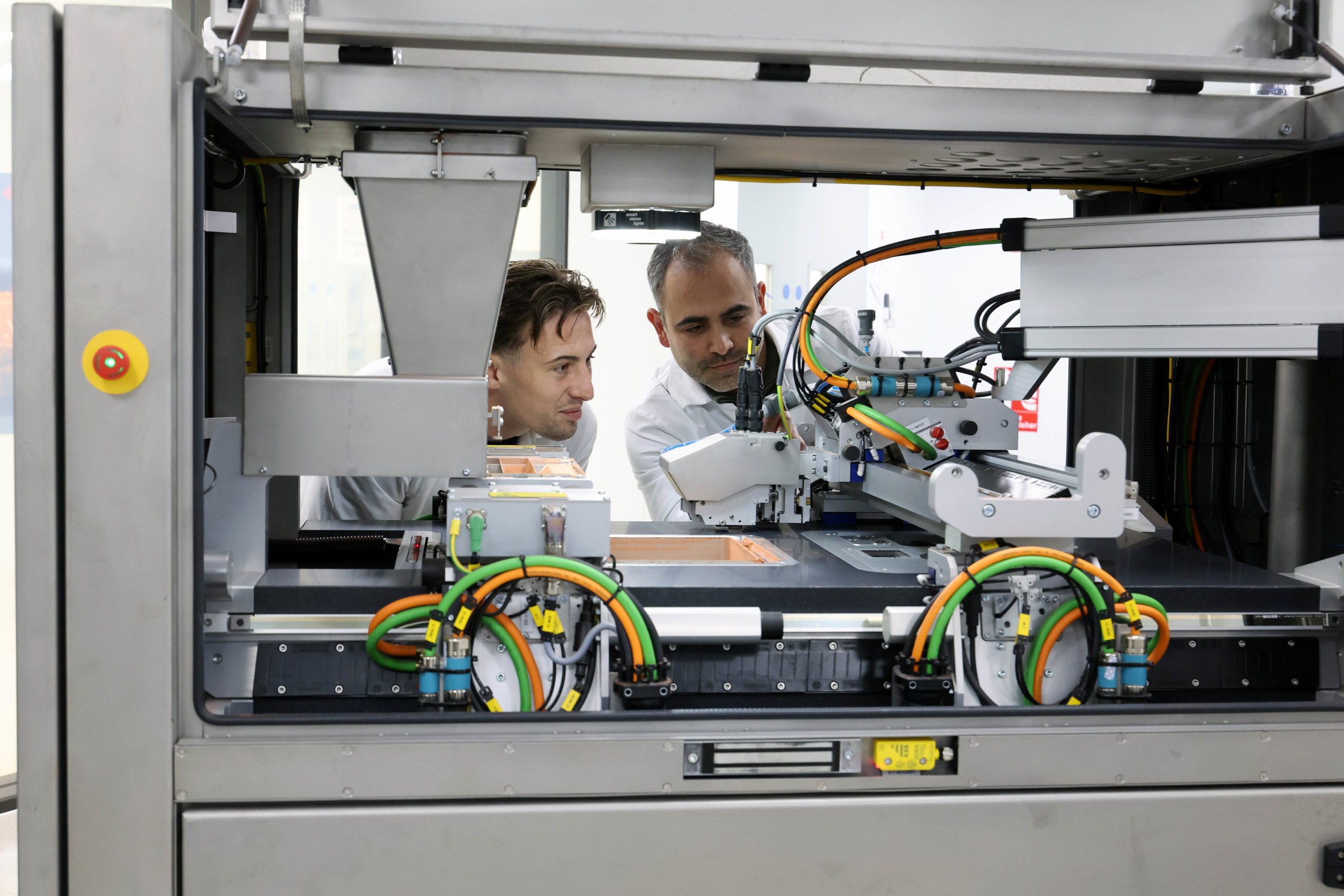 Two men examining industrial machinery with wires and components in a modern factory setting. - CSA Catapult