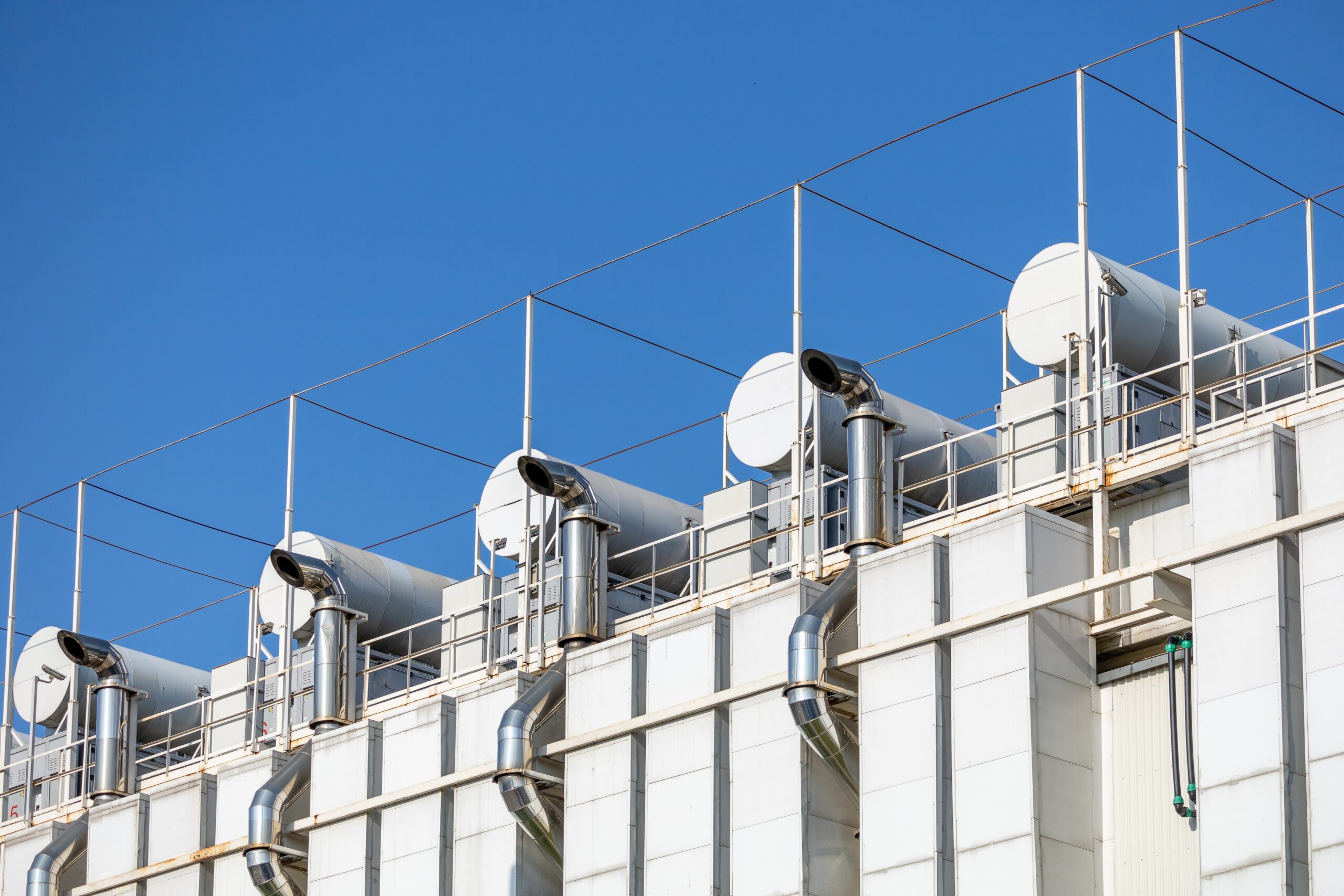 Rooftop view of a data centre's industrial ventilation units against a clear blue sky, with large cylindrical ducts and support rails. - CSA Catapult