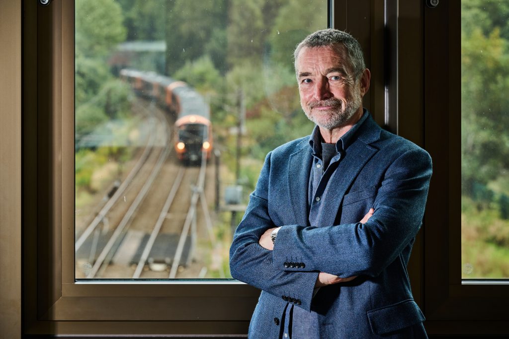 man stood infront of a window that shows a train travelling on the tracks outside