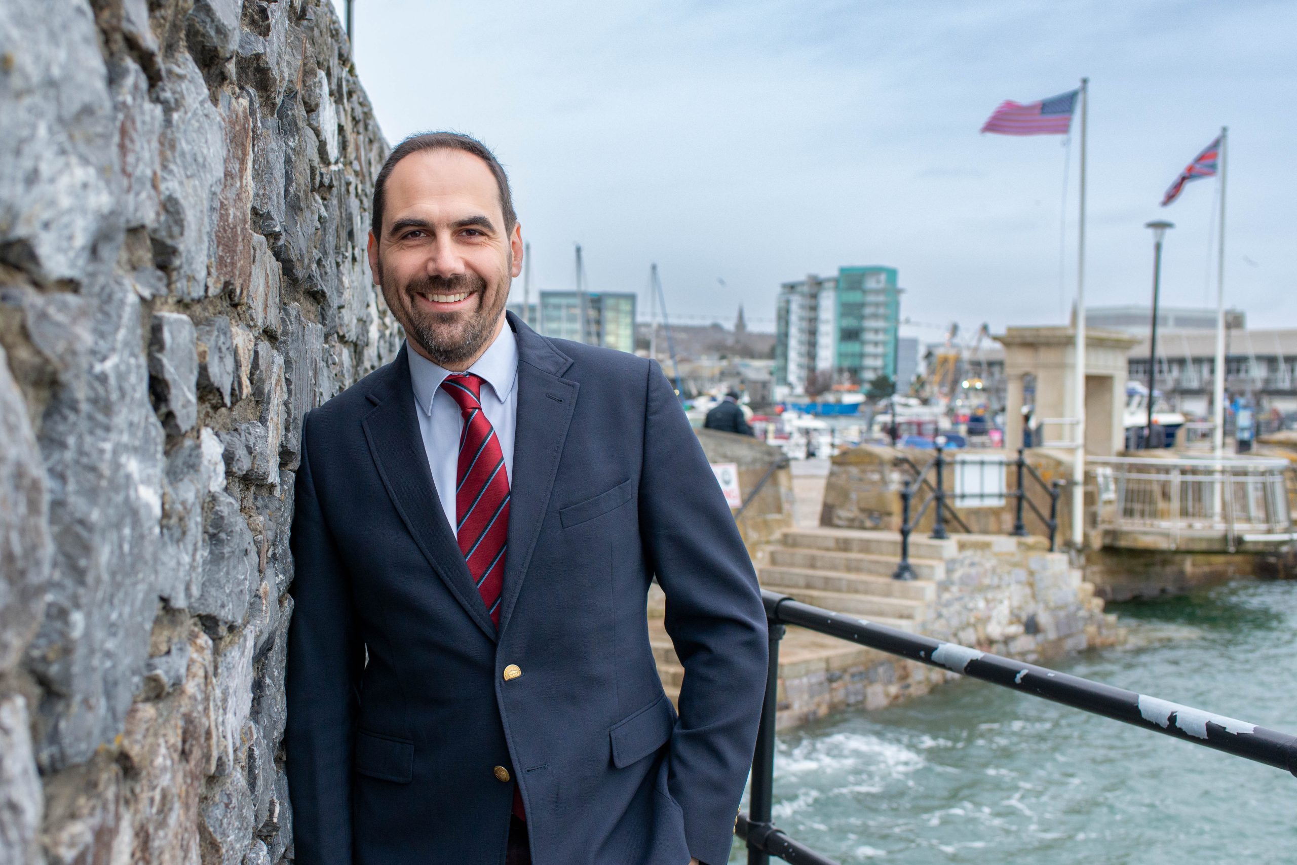 Man in suit standing next to railing looking out on sea in Plymouth