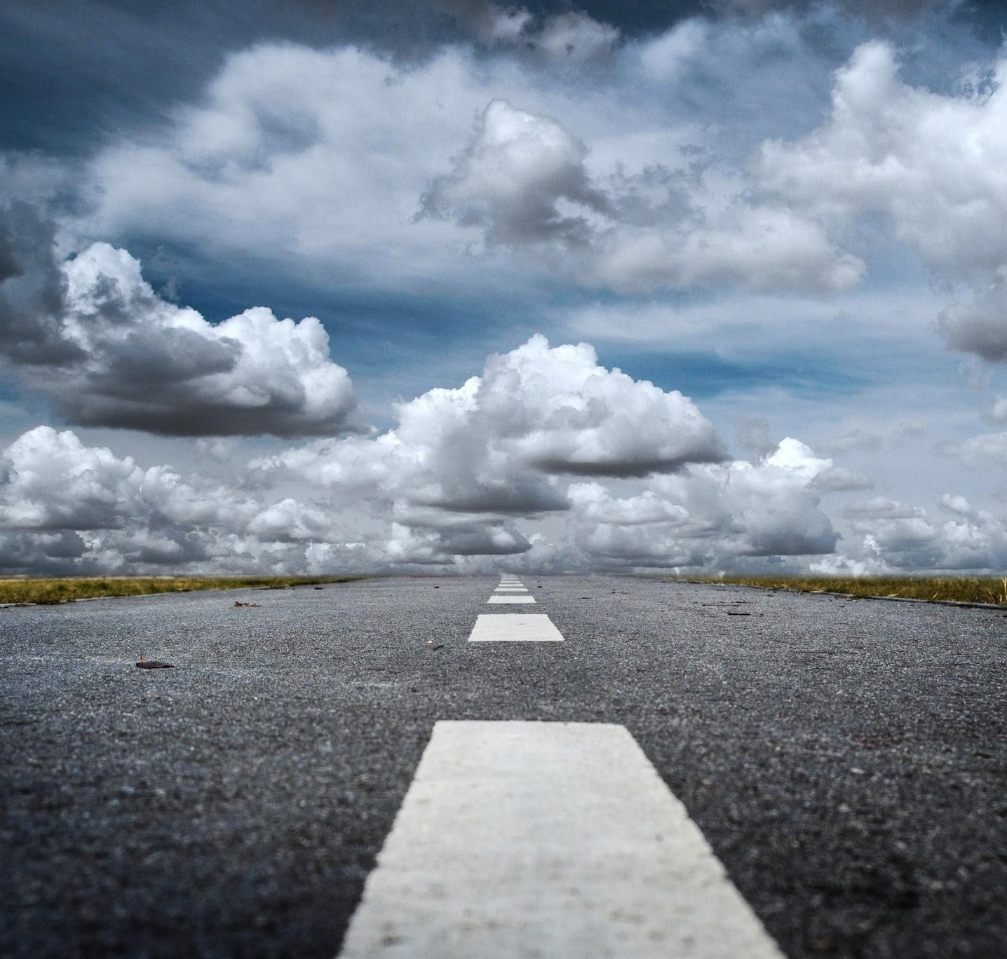 Empty road leading to horizon under a sky filled with fluffy clouds.