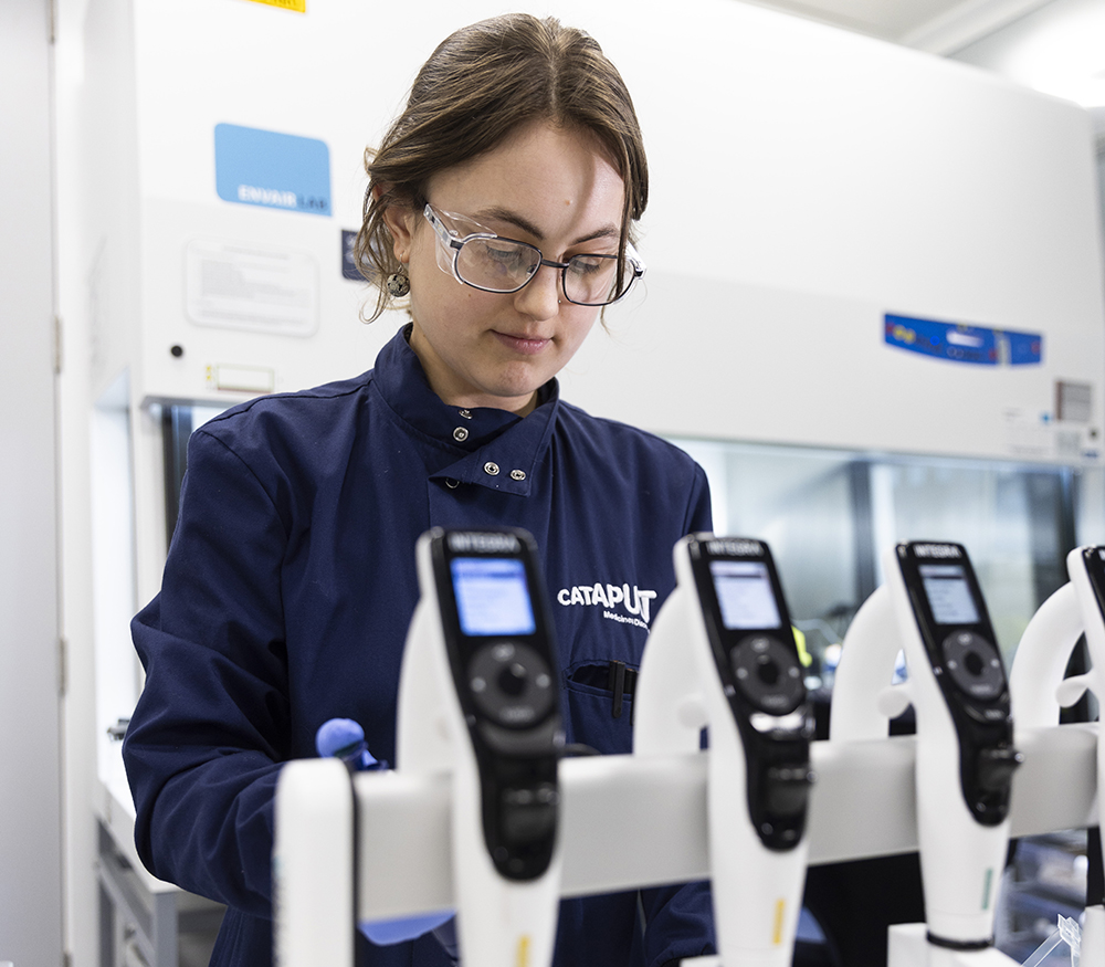 Medicines Discovery Catapult - A scientist works at a bench in a lab with a large safety cabinet in the background