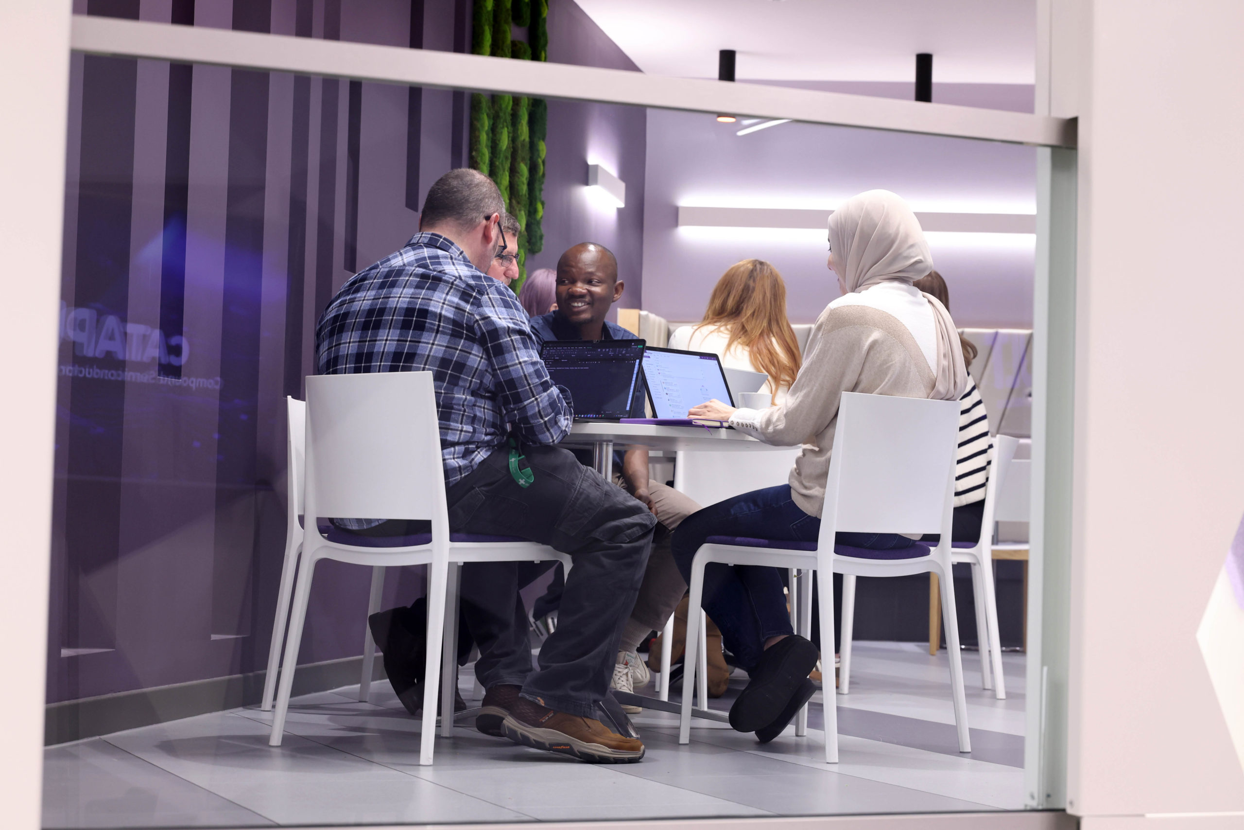 A group of people sit round a table with laptops, collaborating in a modern office space. - CSA Catapult