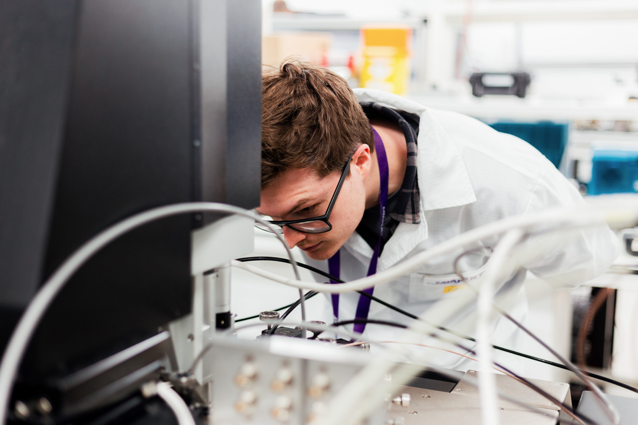 A scientist in a lab coat closely examines equipment in a laboratory setting. - CSA Catapult