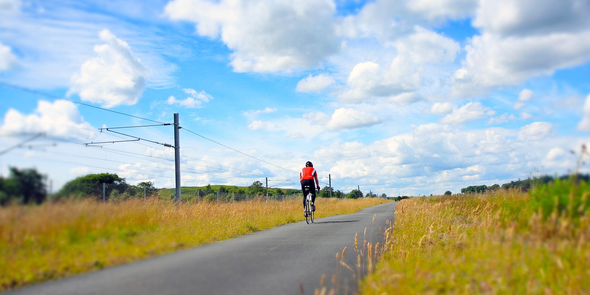 Person cycling along a lane in the summer with a railway in the background. 