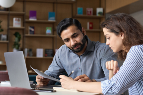 A man and woman sat at a desk in a professional setting, reviewing a document