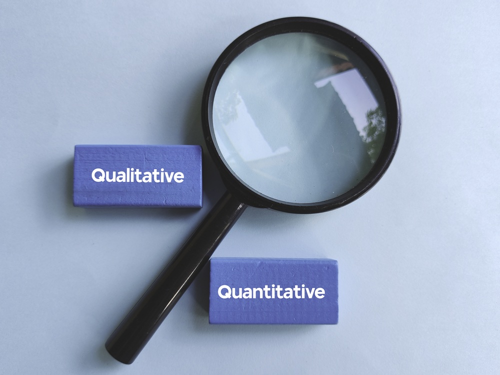 Magifying glass on a blue background. There is a small blue block on either side of the magnifying glass. One block is written 'Quantitative' on the other 'Qualitative'. Credit: iStock Photo