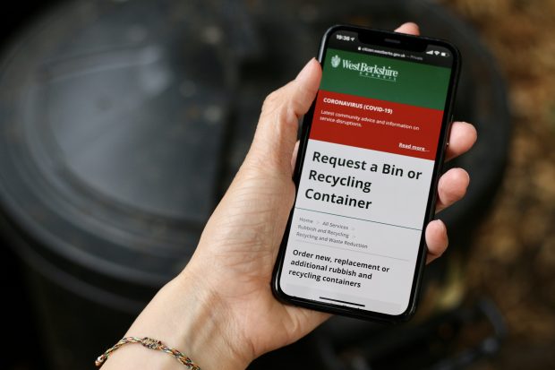 A woman’s hand holding a smartphone with the digital service interface of West Berkshire Council’s Request a bin or recycling container service