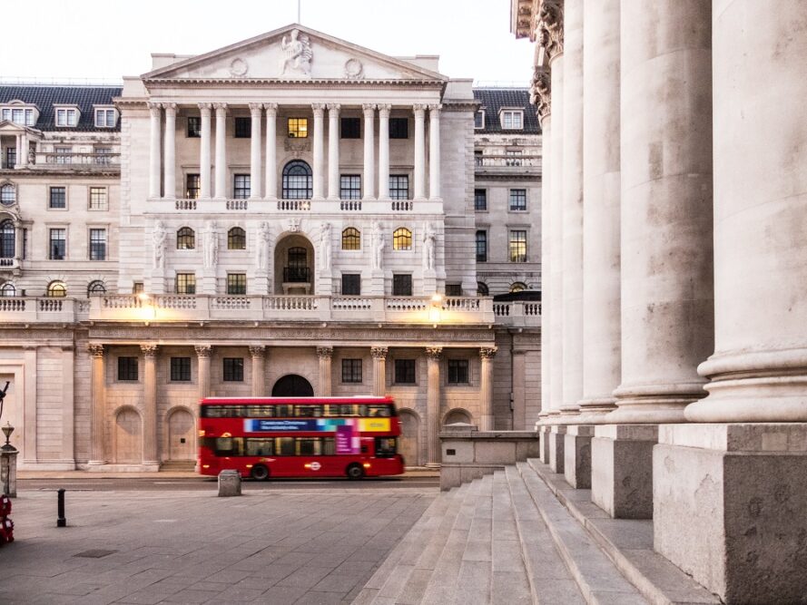 A red double decker bus is seen going past the front of the Bank of England building.