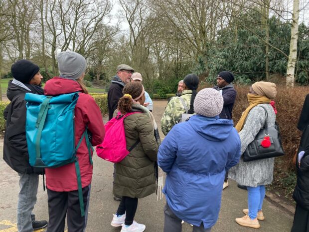 Nature Champions learning how to use apps to identify birds with Yorkshire Wildlife Trust at East Park, Hull. Lots of people are stood around the instructor as he talks them through the workshop. They are all dressed in coats and scarves, indicating it is cold outside