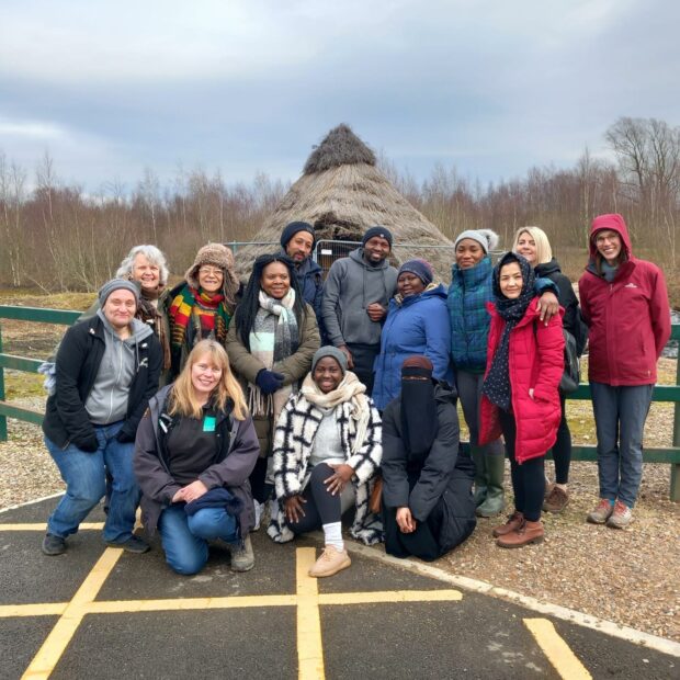 Nature Champions at Natural England’s Humberhead Peatlands NNR learning about Nature Connectedness with Yorkshire Wildlife Trust. The group pose for a photo together in front of a thatched roof hut.
