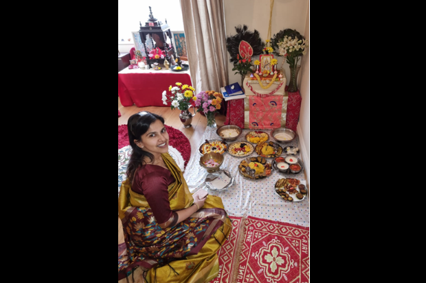 Female, wearing traditional Indian clothing, sitting on the floor which is covered in bowls of food and flowers.