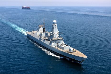 A Royal Navy vessel at sea with a container ship visible in the background.