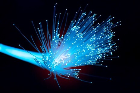 Close-up image of fibre‑optic strands fanning outward, emitting points of blue light against a dark background.